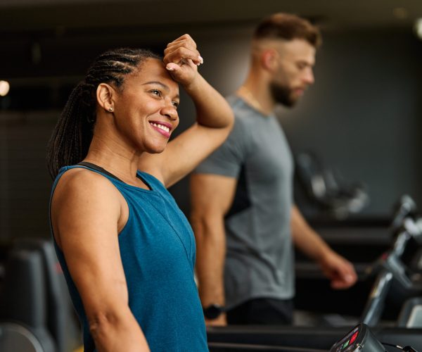 Portrait of a young black woman and white man exercising in a gym, running using  thereadmill machine equipment, healthy lifestyle and cardio exercise resting and taking a break, tired at fitness club concepts